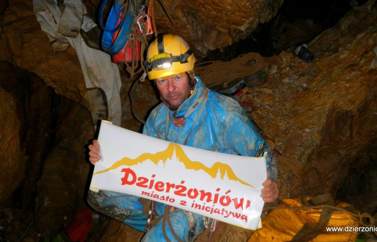 Sławomir Parzonka w jaskini wraz z plakatem "Dzierżoniów miasto z inicjatywą"