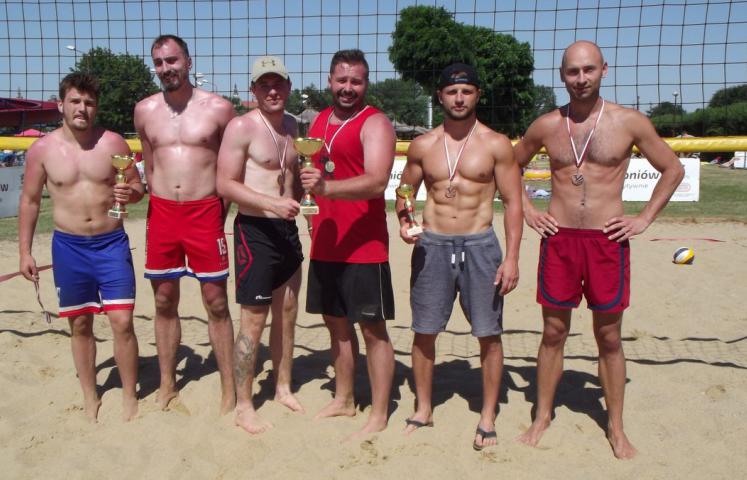 Sześciu zawodników stojących z pucharami na boisku do plażowej piłki siatkowej