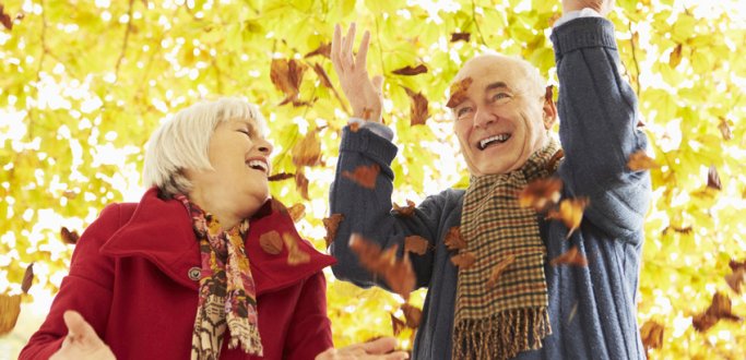 Starsze małżeństwo rozsypuje liście w parku z uśmiechem na usatach