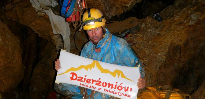 Sławomir Parzonka w jaskini wraz z plakatem "Dzierżoniów miasto z inicjatywą"