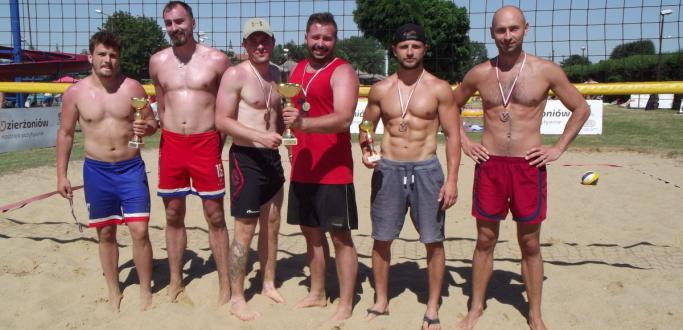 Sześciu zawodników stojących z pucharami na boisku do plażowej piłki siatkowej