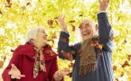 Starsze małżeństwo rozsypuje liście w parku z uśmiechem na usatach